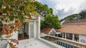 A balcony with a tiled floor, a railing, and a view of a building with a tiled roof. - amã Stays & Trails Chikoo Villa, Goa (Anjuna)