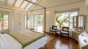 A bedroom with a bed, a ceiling fan, a window with a view, and a chair. - amã Stays & Trails Chikoo Villa, Goa (Anjuna)