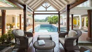 A covered outdoor area with a pool, wicker furniture, and a view of the landscape. - amã Stays & Trails Chikoo Villa, Goa (Anjuna)