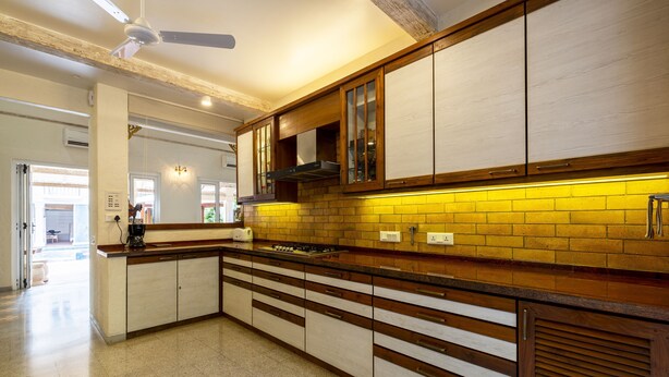 A modern kitchen with wooden cabinets, a tiled backsplash, and a central island. - amã Stays & Trails Chikoo Villa, Goa (Anjuna)