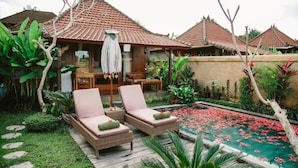 A traditional house with a tiled roof, a swimming pool with red flowers, and two lounge chairs with cushions. - Niluh Private Villas (Ubud)