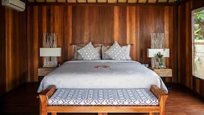A wooden-paneled room with a bed, two nightstands, and a bench. - Niluh Private Villas (Ubud)