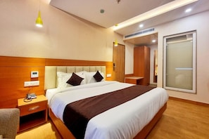 Quarto de hotel com cama, mesa de cabeceira, luminária e armário.