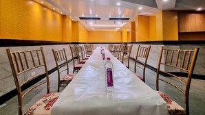 Una larga mesa de banquete con sillas, una botella de Sprite y un mantel corrido floral en una habitación con paredes y luces de techo amarillas.