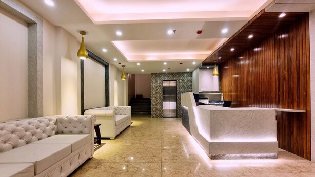 Un hall de hotel con mostrador de recepción, zona de estar y una escalera que conduce a un ascensor.