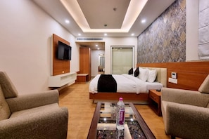 Quarto de hotel com cama, duas poltronas, uma televisão e uma pequena mesa com uma garrafa.