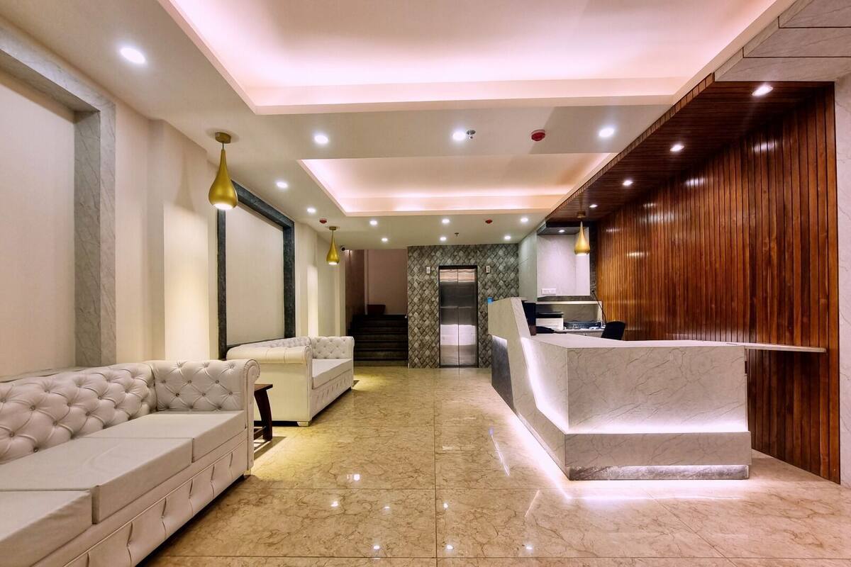 A hotel lobby with a reception desk, seating area, and a staircase leading to an elevator.