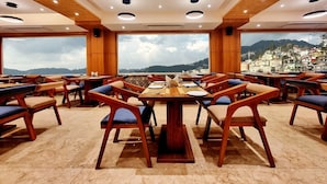 A restaurant with wooden tables and chairs, large windows, and a view of a mountainous landscape. - Mountain Valley View By Terraa (Shimla)