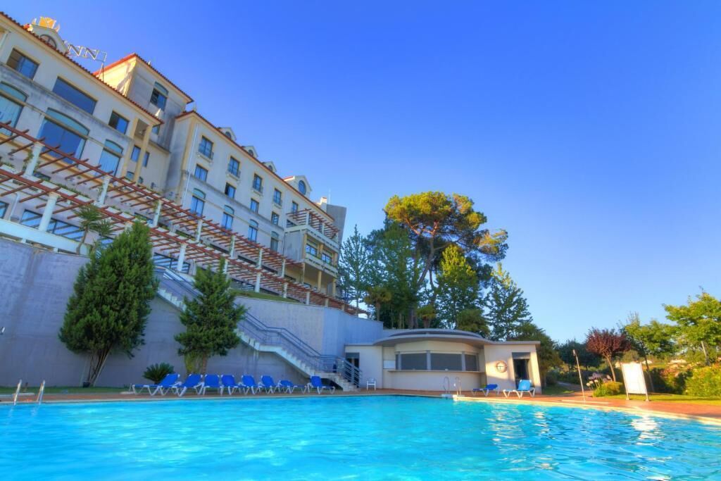 Una piscina con sillas de descanso, un edificio de varios pisos y una escalera que sube a un nivel superior.