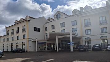 A hotel entrance with a covered area, multiple windows, and a parking lot with cars.