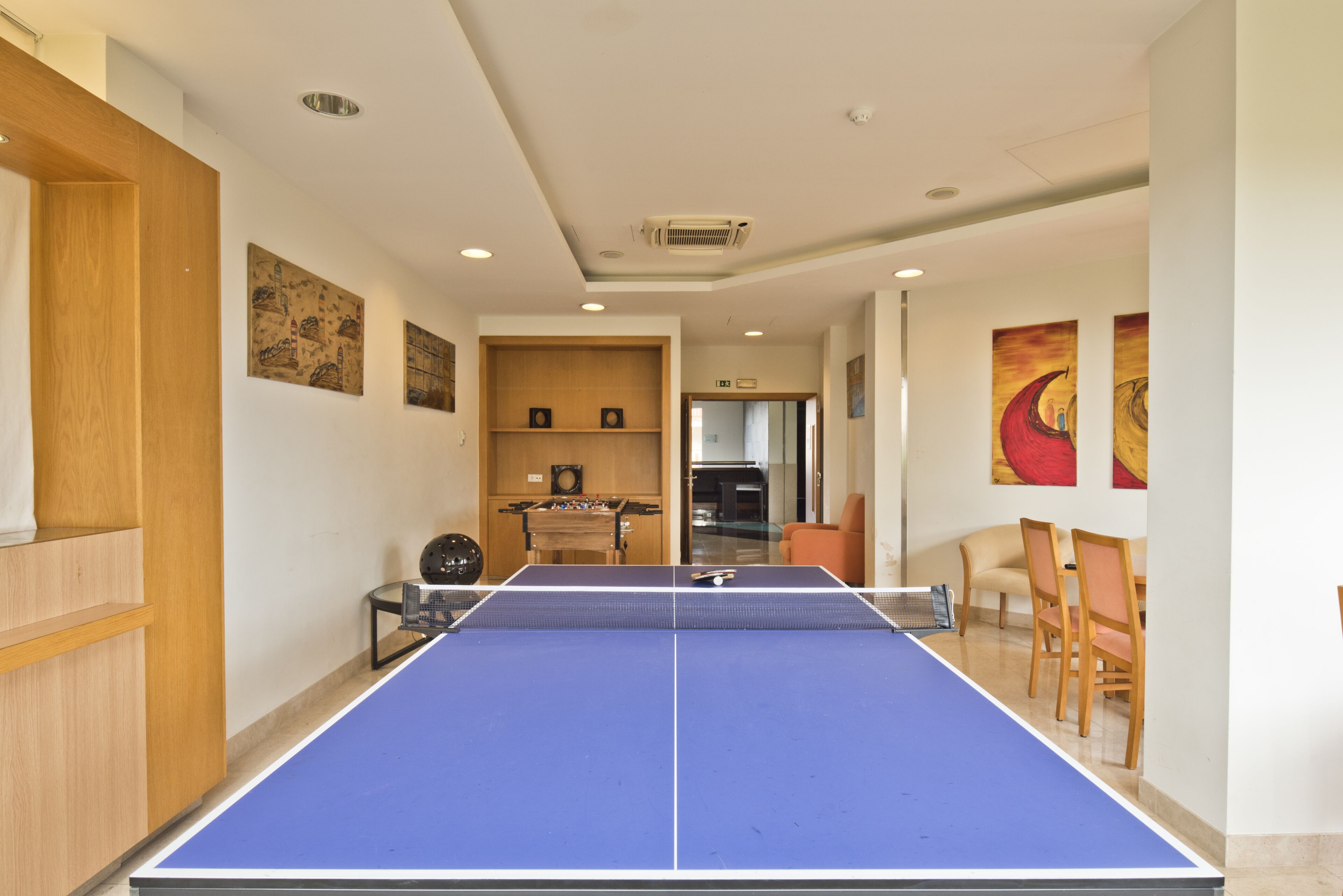 A room with a ping pong table, wooden furniture, and artwork on the walls.