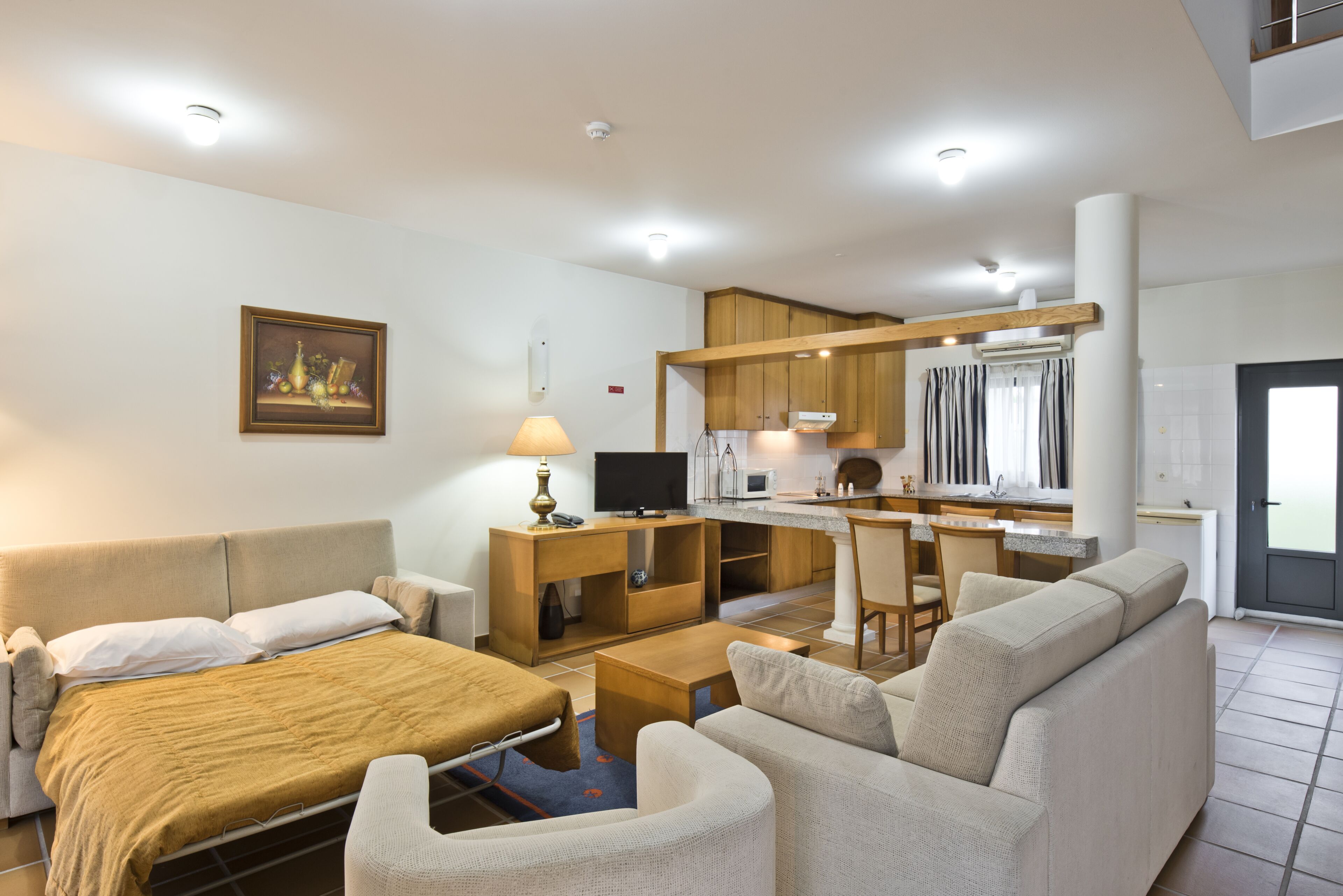 Una habitación de hotel moderna con cama, sofá, televisión, kitchenette y zona de comedor.