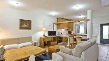 Una habitación de hotel moderna con cama, sofá, televisión, kitchenette y zona de comedor.