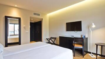 Una habitación de hotel con cama, escritorio, silla, televisión y lámpara.