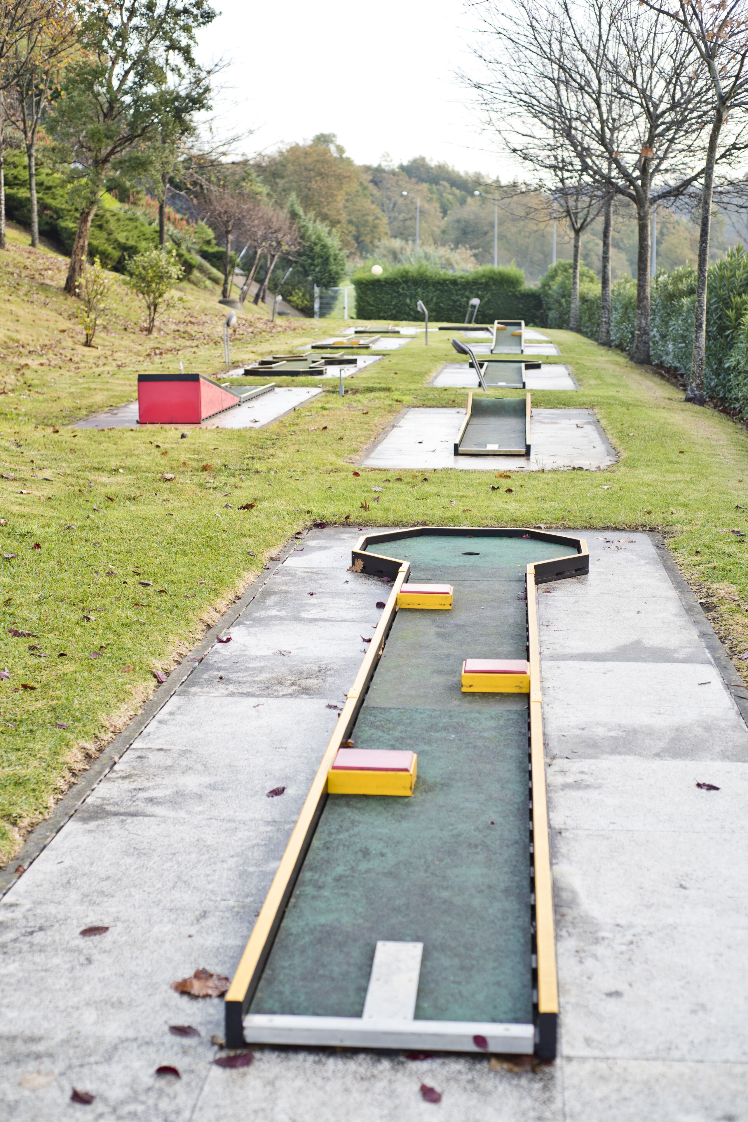Een minigolfbaan met een groen puttingoppervlak, gele en rode obstakels, en een rood gebouw op de achtergrond.