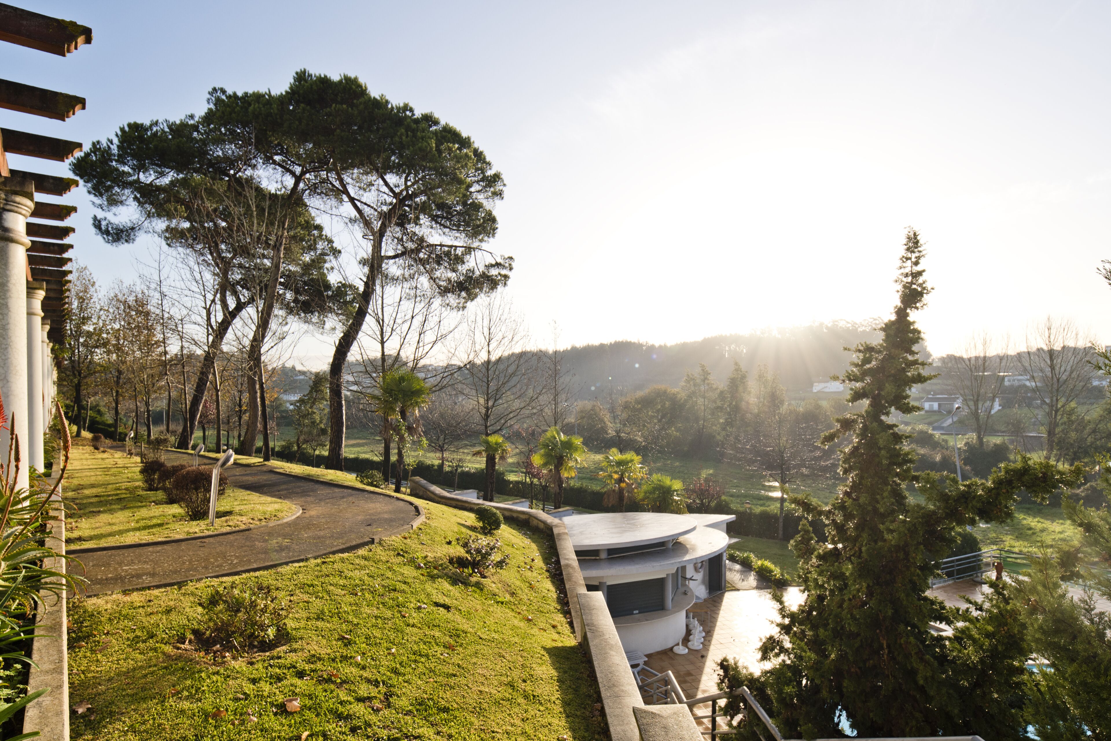 A modern building with a curved roof, surrounded by a landscaped garden with pathways and trees.