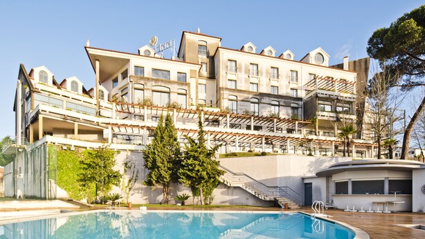 Un hotel moderno con piscina, varios balcones y un jardín ajardinado.