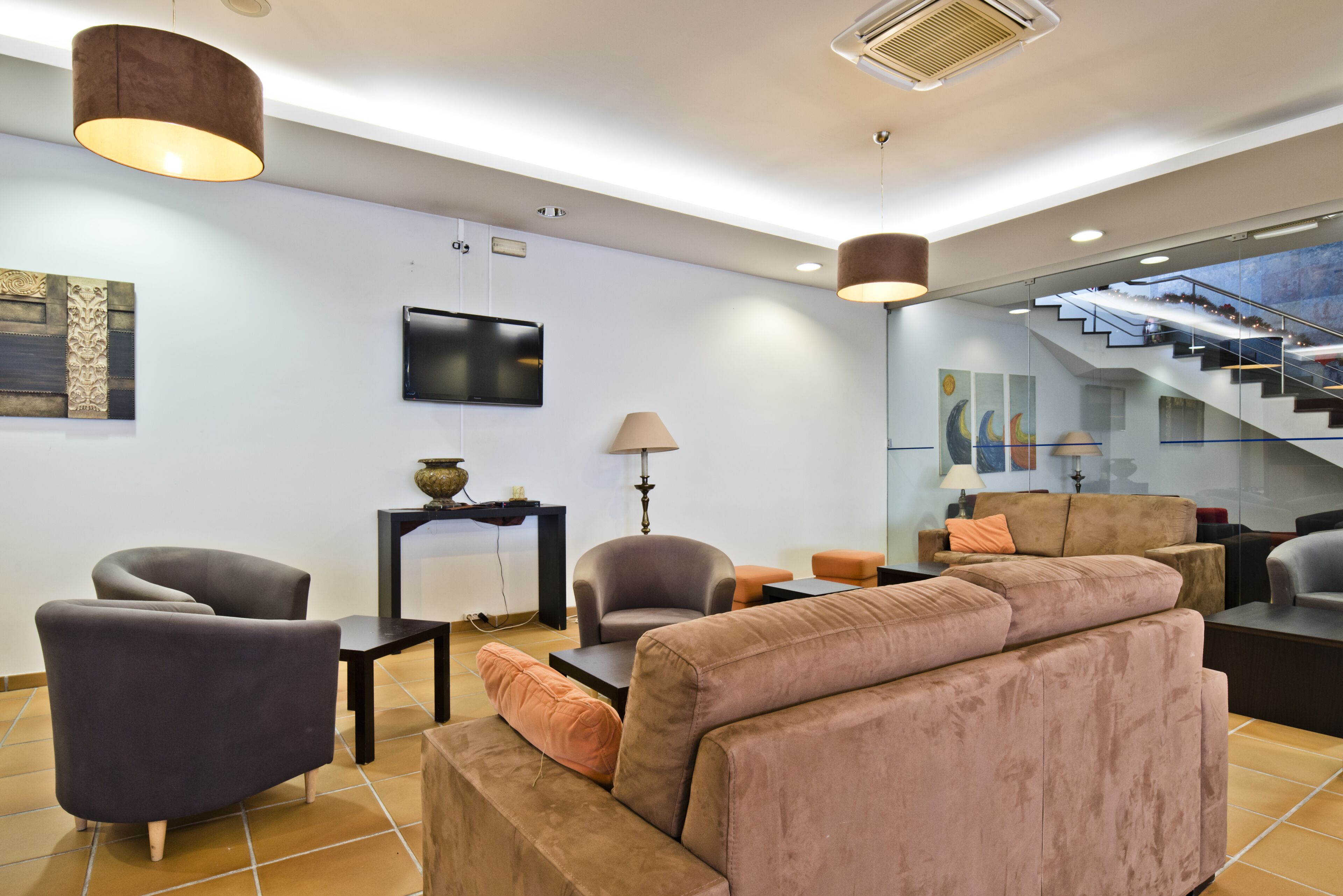 A modern living room with a sofa, armchairs, a TV, and a staircase.