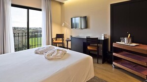 Habitación de hotel con una cama grande, un escritorio, un televisor y un balcón con vistas.