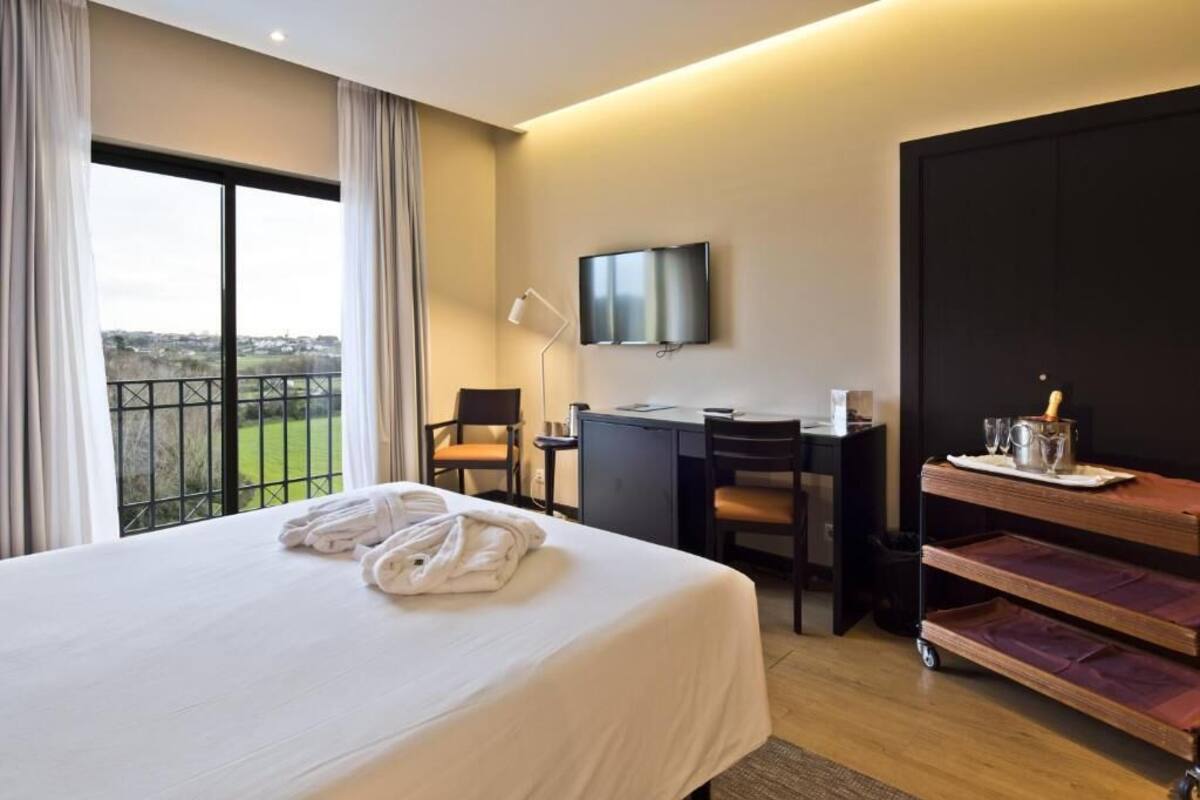 A hotel room with a large bed, a desk, a TV, and a balcony with a view.