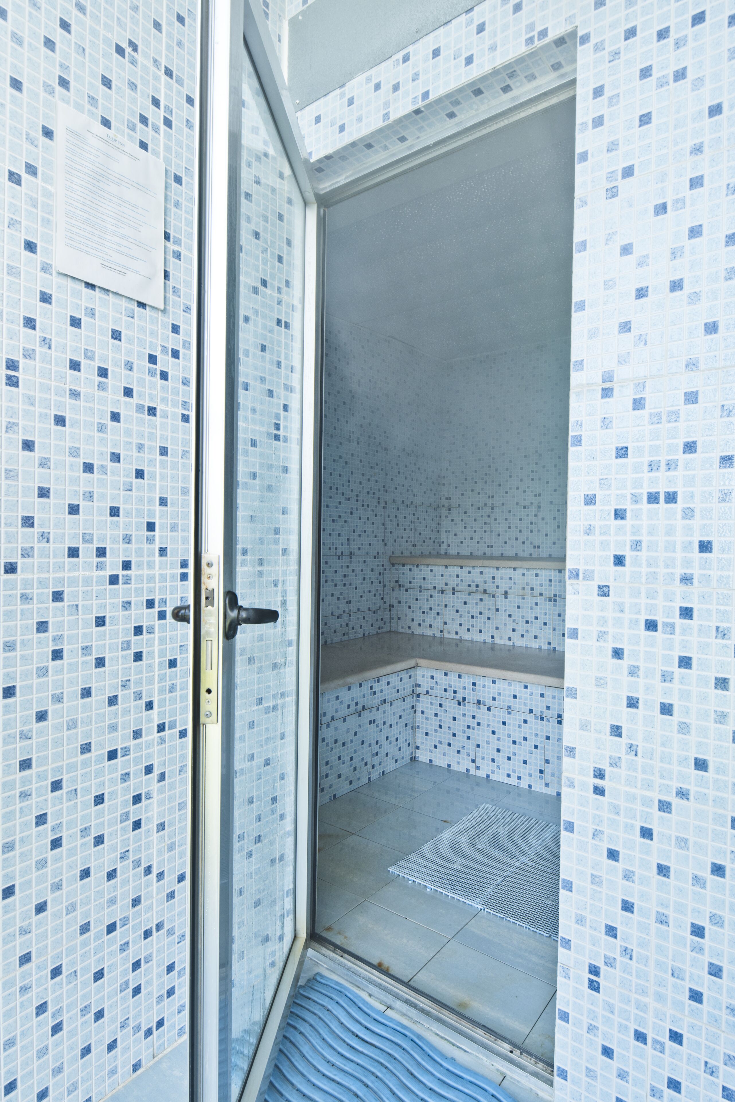 Une salle de bain avec un mur carrelé, un espace douche et une porte dotée d’une poignée.