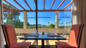 Una terraza con mesa y sillas, vista a zonas verdes y colinas, y una estructura de pérgola.