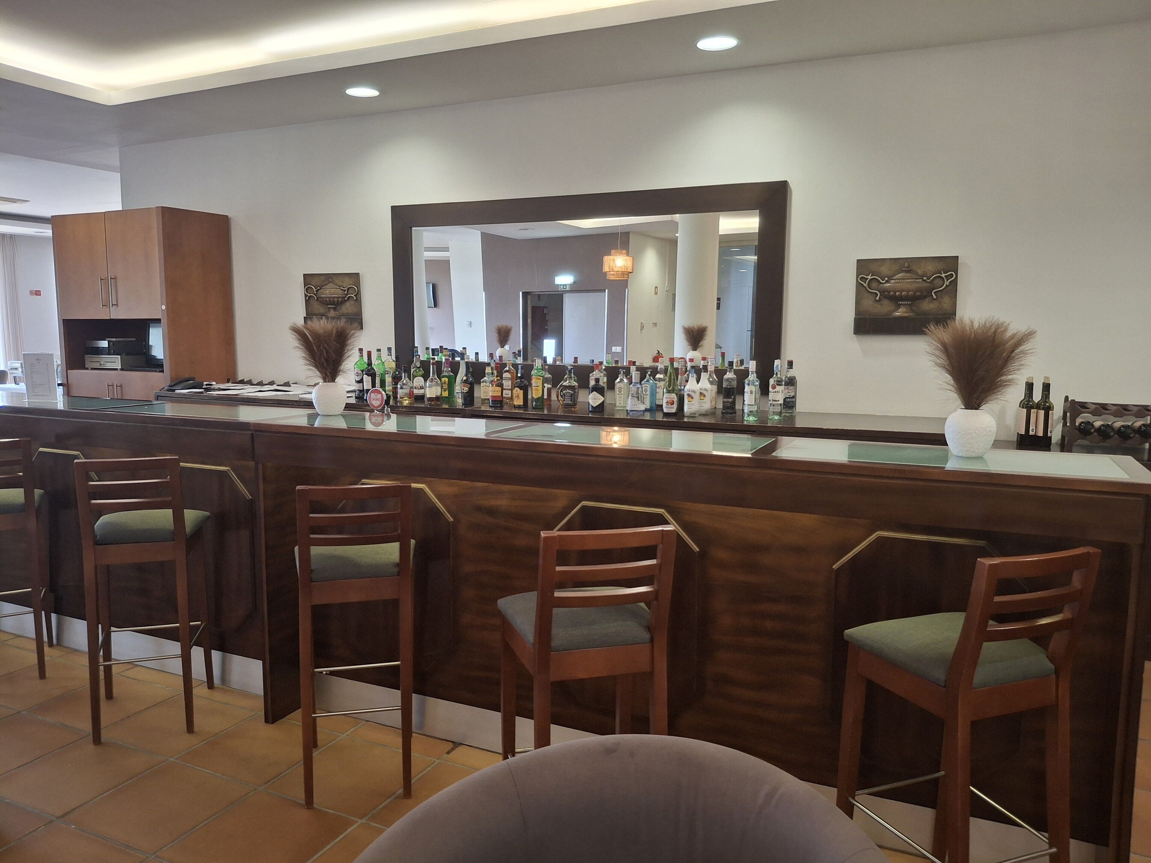 A bar area with a wooden counter, multiple chairs, a large mirror, and a variety of bottles.