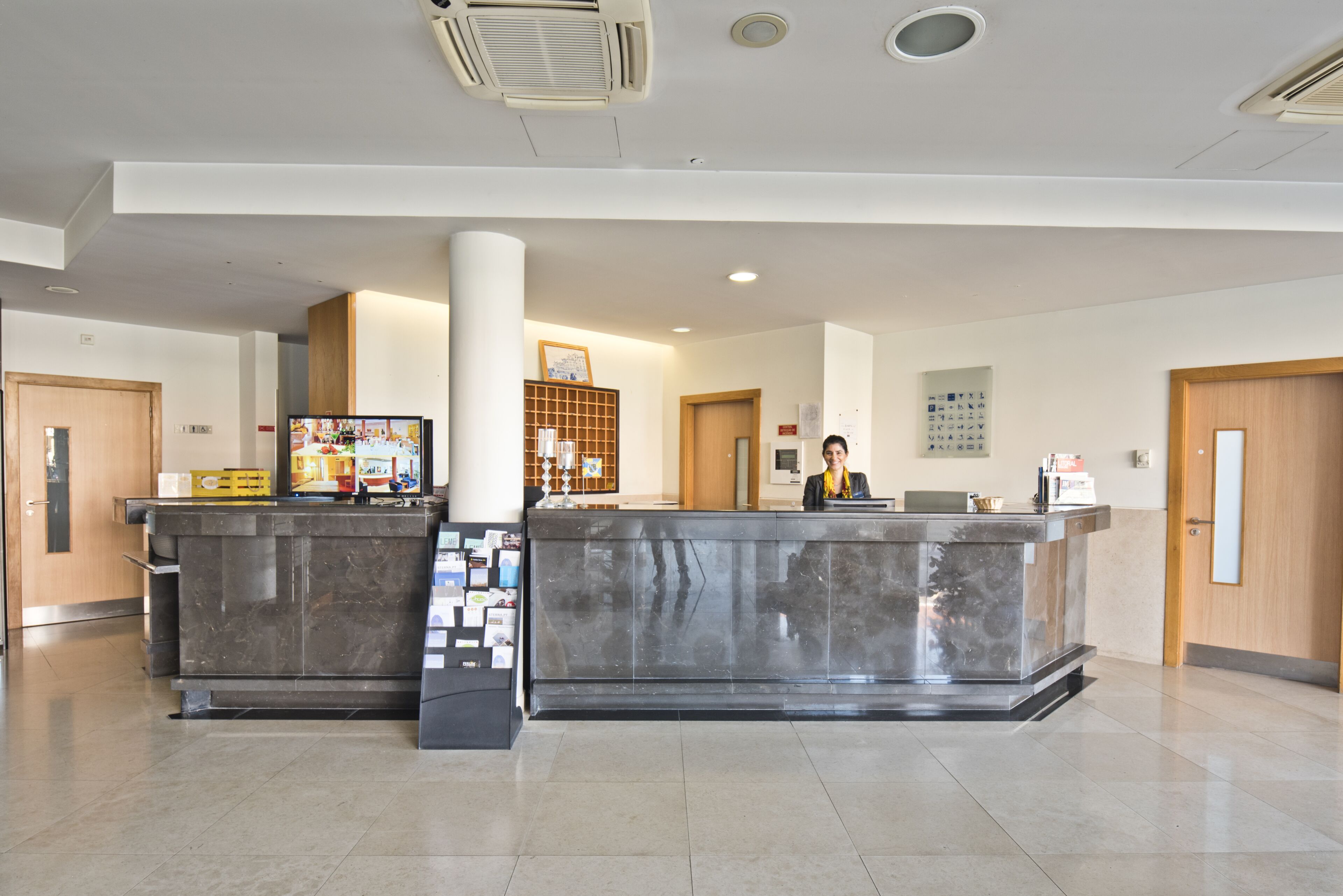 A reception desk with a receptionist, a wooden door, a bulletin board, and a wall-mounted clock.