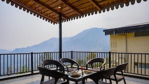 Ein Balkon mit vier Korbstühlen, einem Tisch mit Teekanne und Speisen sowie Blick auf die Berge.