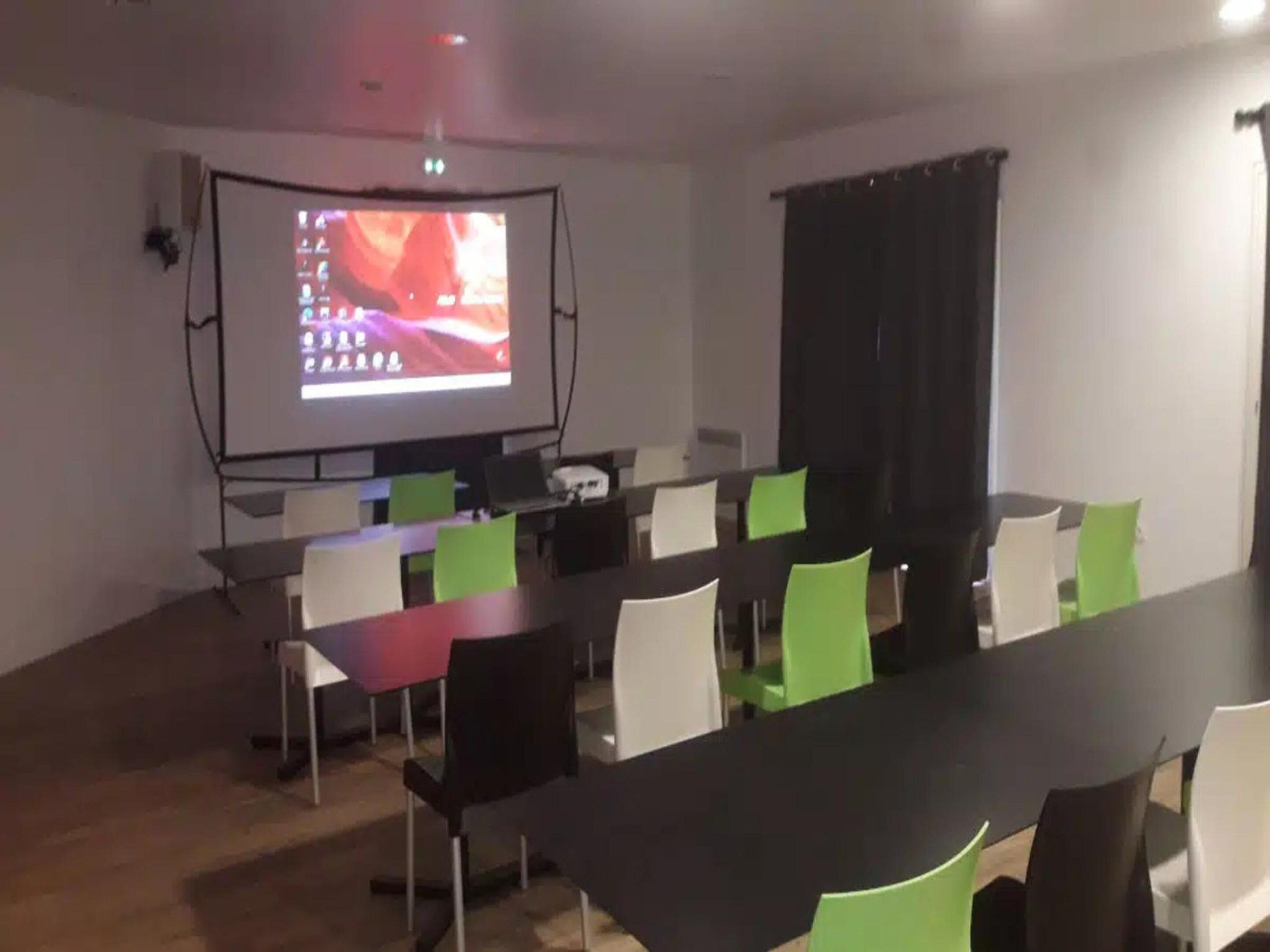 A conference room with a projector screen, tables, and chairs.