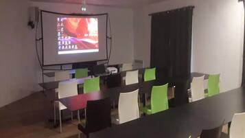 A conference room with a projector screen, tables, and chairs.