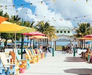 A beachside seating area with colorful chairs and umbrellas, a covered seating area with a sign, and a view of the sea.