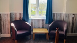 A room with two armchairs, a small wooden table, and a window with blue curtains.
