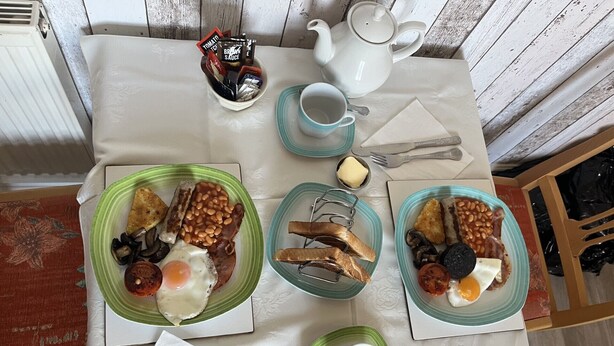 A breakfast table with plates of eggs, beans, sausages, and toast.