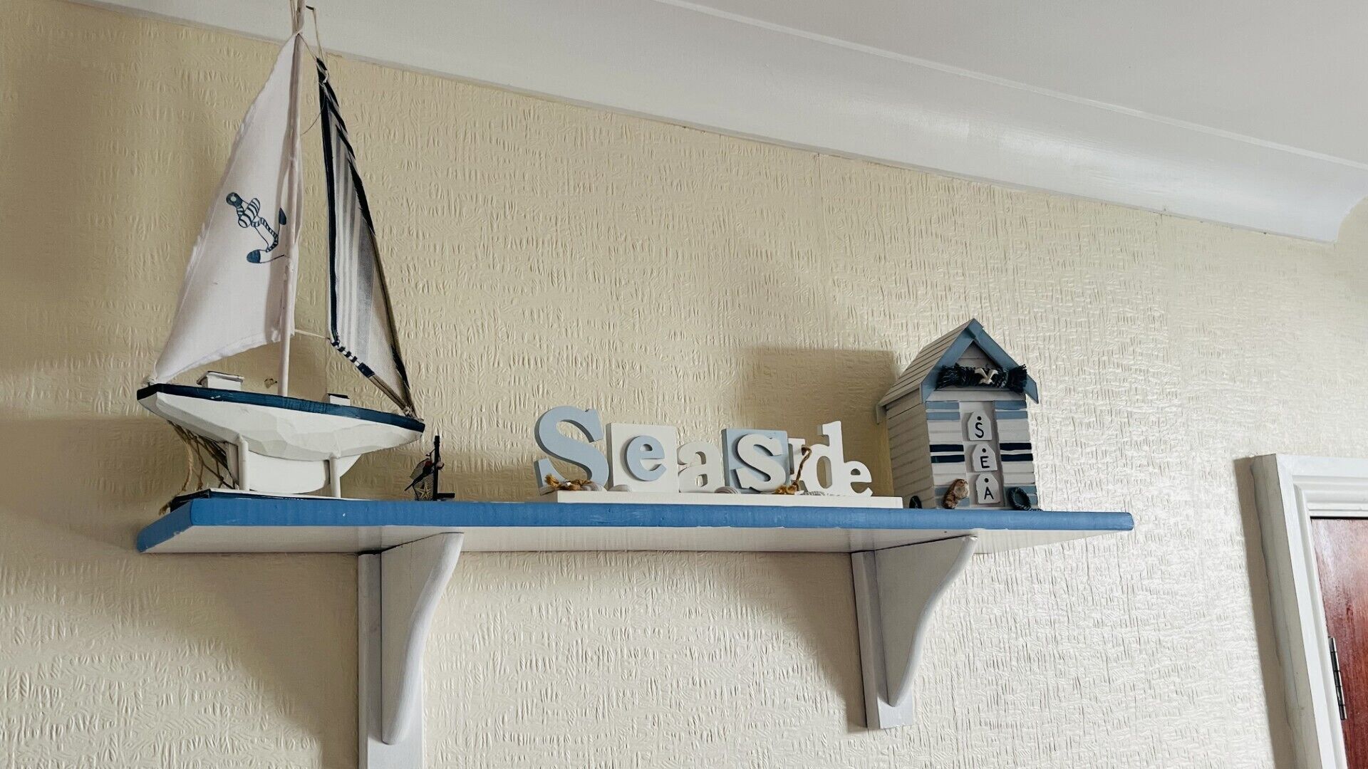 A shelf with a sailboat model, the word 'Seaside,' and a small house model.
