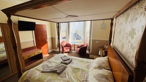 A four-poster bed with a canopy, two armchairs, a small table, and a television in a hotel room.