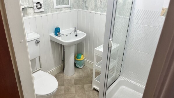Et lille badeværelse med toilet, håndvask og brusebad.