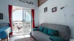 Et værelse med en grå sofa, et træsidebord, en gulvtæppe med mønster, et spisebord med stole og en skydedør, der fører til et udendørs område.