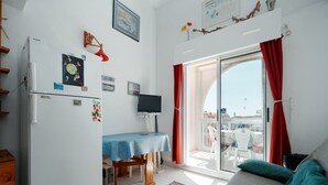 En kompakt opholdsstue med tekøkken, spiseplads med bord og stole, sofa samt skydedør til et udendørs område.