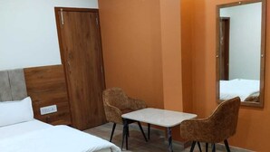 Una habitación de hotel con cama, una mesita, dos sillas, un armario y un espejo.