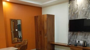 Habitación de hotel con cama, armario de madera, escritorio con silla, televisor montado en una pared de mármol y ventilador de techo.