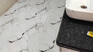 Un baño con lavamanos blanco, encimera negra y suelo de mármol con una pared también de mármol negro.