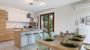 Ett modernt kök med en central köksö, barstolar och ett matbord med plats för sex personer, komplett med tallrikar och glas.