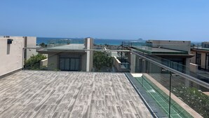 En takterrass med utsikt över havet, modern arkitektur och ett glasräcke.