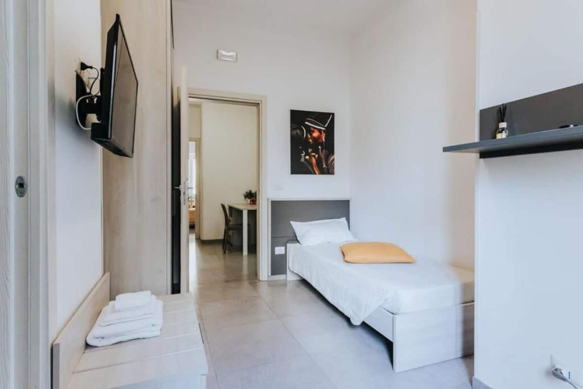 Een moderne hotelkamer met een bed, een aan de muur bevestigde televisie, een schilderij en een plank met een fles.