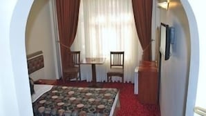 Una habitación con una cama, una mesita, dos sillas y un ventanal con cortinas.