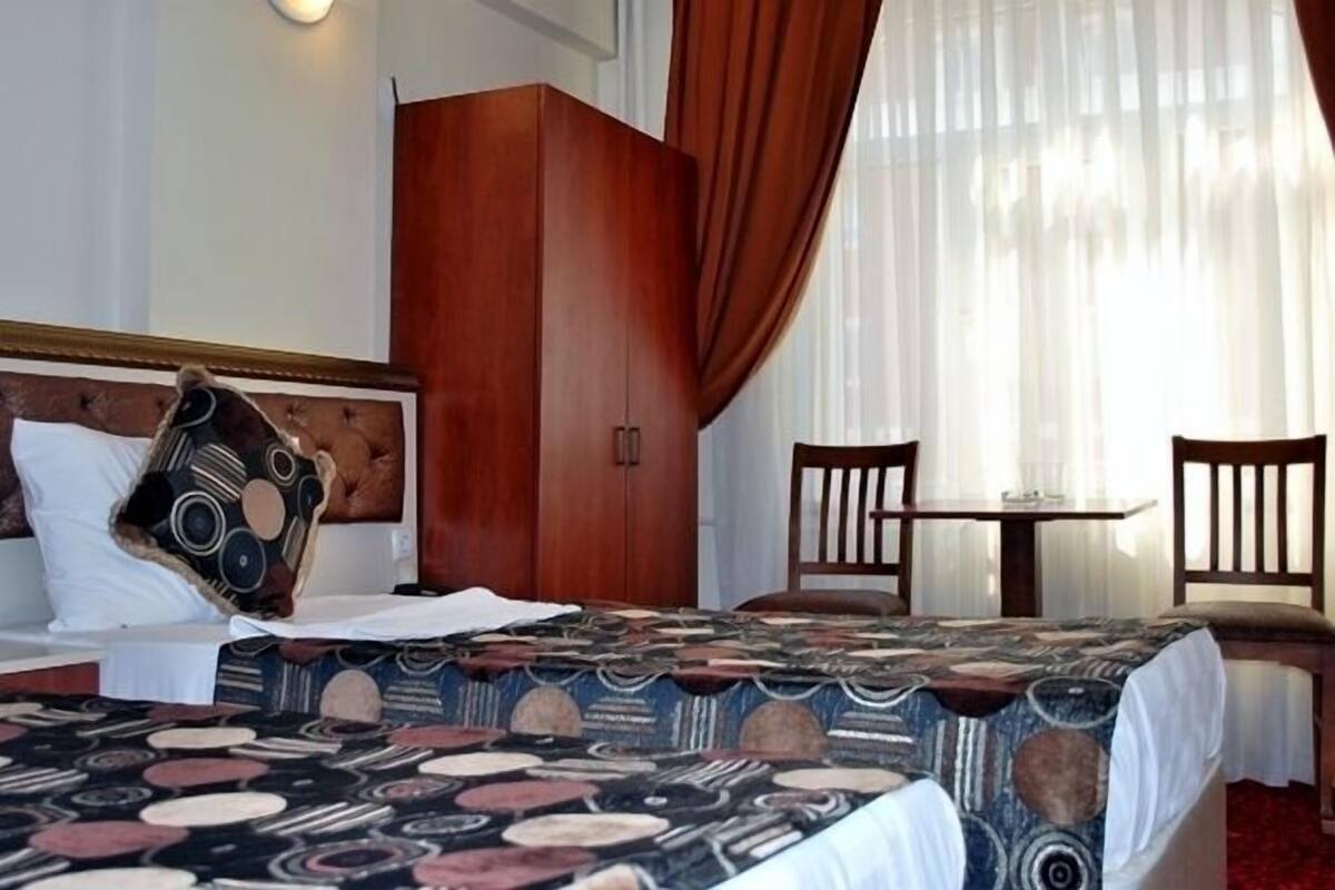 A hotel room with a bed, a wooden wardrobe, a small table, two chairs, and a window with curtains.