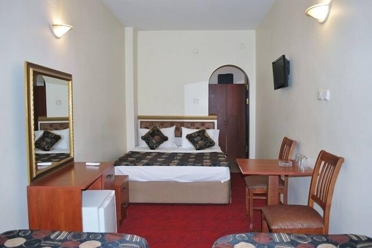 A hotel room with a bed, a desk, a chair, a mirror, and a TV.