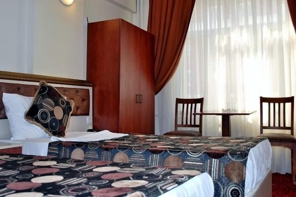 A hotel room with a bed, a wooden wardrobe, a small table, two chairs, and a window with curtains.