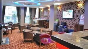 Un vestíbulo de hotel con suelo alfombrado, zona de estar con sillones, un mostrador de recepción y una pantalla de televisión.